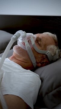 Mature adult sleeping at night while wearing a CPAP mask to treat his Sleep Apnea. Vertical Video.