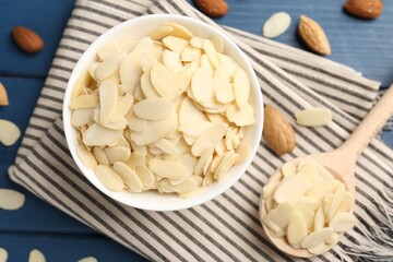 Fresh almond flakes and whole nuts on blue wooden table, flat lay