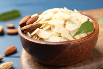 Fresh almond flakes, whole nuts and green leaf on blue table, closeup