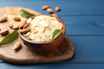 Fresh almond flakes, whole nuts and green leaves on blue wooden table, closeup. Space for text