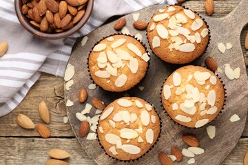 Tasty muffins with almond flakes and nuts on wooden table, flat lay
