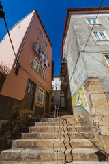 A steep, sunlit stone staircase winds through a narrow alley between weathered buildings