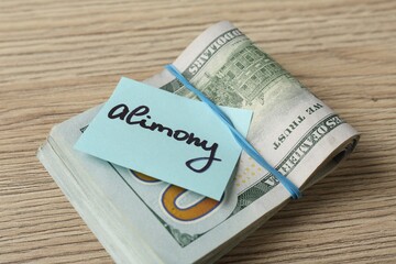 Note with word Alimony and money on wooden table, closeup