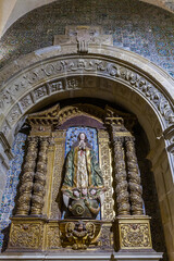 An ornate, gilded altarpiece featuring a statue of a robed figure stands beneath a stone arch