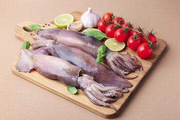 Fresh raw squids, tomatoes, lime and spices on beige table, closeup