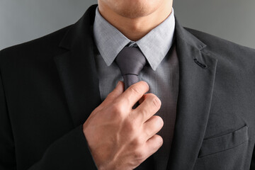 Man in suit adjusting his necktie on grey background, closeup