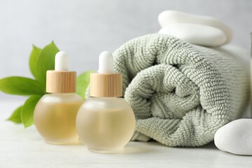 Essential oils, towel, spa stones and green leaves on white table, closeup