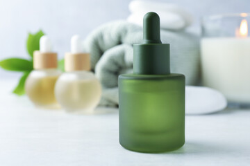 Essential oils, towel, spa stones, burning candle and green leaves on white table, closeup. Space for text