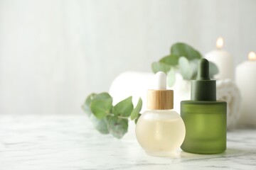 Beautiful spa composition with essential oils and eucalyptus on white marble table, closeup. Space for text