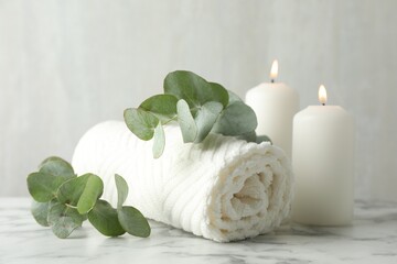 Soft towel, burning candles and eucalyptus leaves on white marble table, closeup