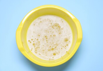 Yellow plastic basin with water and foam on light blue background, top view