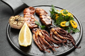 Tasty cooked squids served with lemon, garlic and salad on black table, closeup