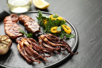 Tasty cooked squids served with garlic and salad on black table, closeup