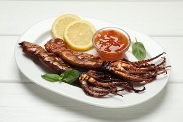 Tasty cooked squids served with lemon, sauce and basil on white wooden table, closeup