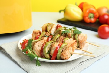 Tasty skewers with chicken, vegetables, parsley and air fryer on white table, closeup