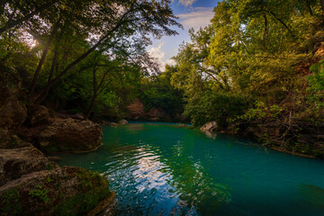 Turquoise river with steep rocky bank at sunset, lush forest landscape