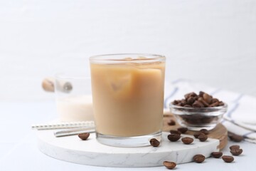 Tasty iced coffee with milk and beans on white table