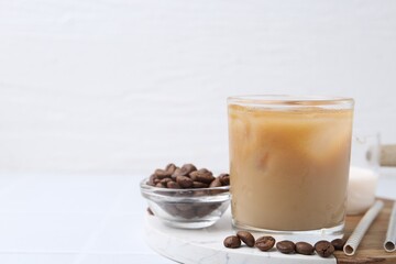 Tasty iced coffee with milk and beans on white table. Space for text