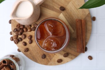 Tasty iced coffee in glass, milk and beans on white tiled table, flat lay