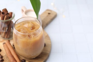 Tasty iced coffee in glass and beans on white tiled table, closeup. Space for text