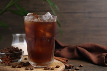 Tasty iced coffee in glass and beans on wooden table, closeup. Space for text