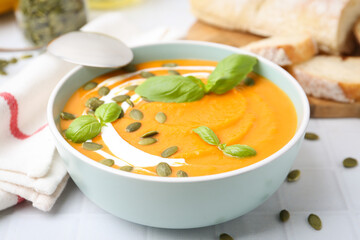 Delicious pumpkin soup served on white tiled table, closeup