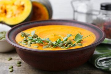 Delicious pumpkin soup with seeds and microgreens in bowl on wooden table, closeup