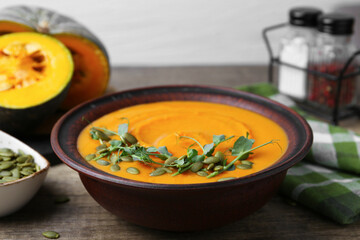 Delicious pumpkin soup with seeds and microgreens in bowl on wooden table, closeup