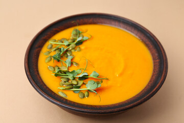 Delicious pumpkin soup with seeds and microgreens in bowl on beige table, closeup