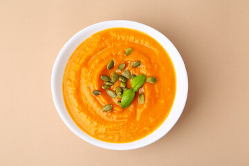 Delicious pumpkin soup with seeds and basil in bowl on beige table, top view