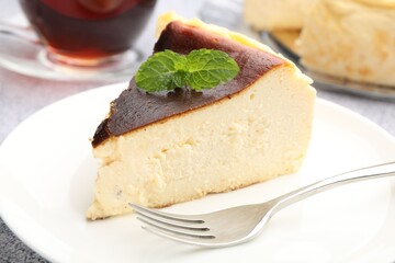 Piece of delicious Basque cheesecake with mint and tea on table, closeup