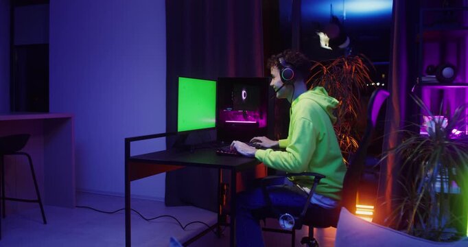 A teenager plays computer games while sitting in front of a monitor with a green screen