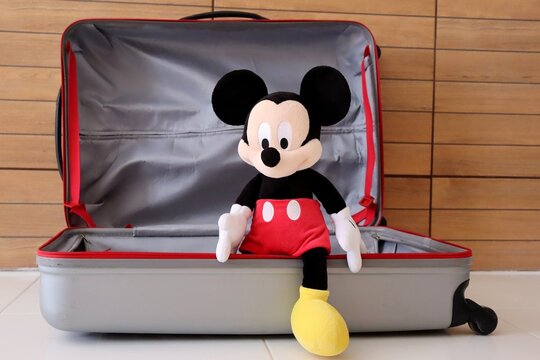 Mickey Mouse toy inside a big luggage bag. Concept of family travel, Disney vacation planning. 
