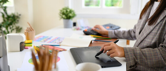 Cropped shot graphic designer working on creative desk computer while using graphic tablet at desk