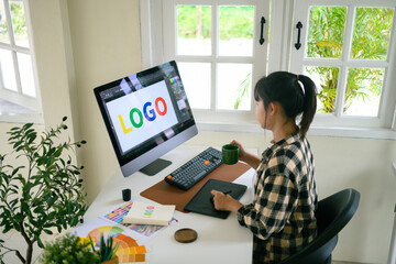 Graphic designer creating logo on digital tablet in bright modern workspace with computer and color palette