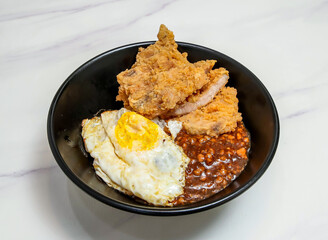 Crispy Fried Pork Chop, Sunny Side Up Egg, and Minced Pork Gravy on Rice in Black Bowl on marble background top view of hang kong food