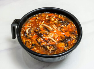 Classic Chinese Hot and Sour Soup in a Black Bowl with Carrots, Wood Ear, tofu and Egg Ribbons on marble background top view of hang kong food