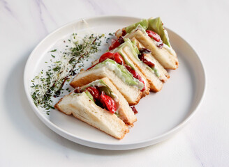 Club Sandwich Halves with Tomato, Lettuce, and Creamy Sauce on White Plate isolated on marble background top view of fast food