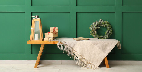 Bench with Christmas wreath, gift boxes and blanket near green wall