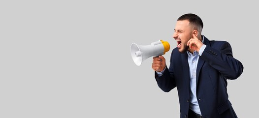 Irritated businessman shouting into megaphone on grey background with space for text