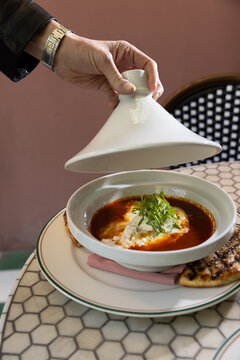 Waiter hand opening a tagine dish to reveal brunch shakshuka at a moroccan themed restaurant
