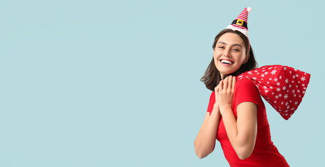 Beautiful young woman in pajamas with Santa Claus bag on blue background