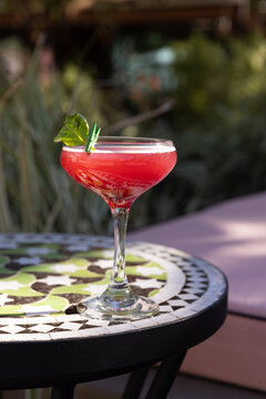 Red handmade cocktail with bail garnish on a tile table poolside 