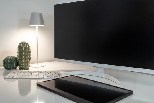 A graphic designer's clean and modern desk with a blank monitor and tablet for mockups