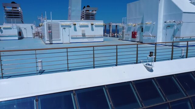 A bright upper deck of a cruise ship with lounges and outdoor seating set between funnels and staircases, and a blue ocean horizon. An ideal visual for travel, luxury, vacation and maritime lifestyle.