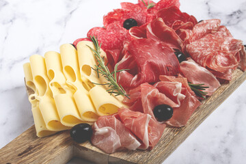 Assorted meat, appetizer, prosciutto, salami and ham, with maasdam cheese and olives, on a wooden board, breakfast, top view, close-up, no people