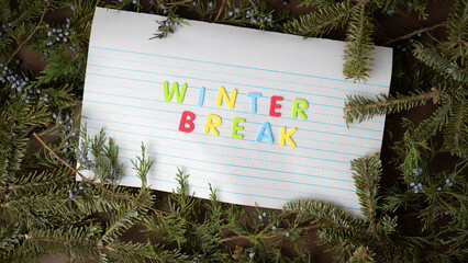 School Winter Break concept with colorful foam letters on lined notebook paper surrounded by evergreen tree branches.