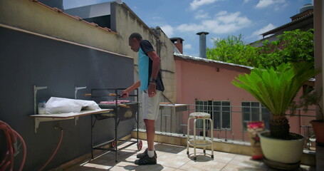 African American man grilling meat on a rooftop terrace, preparing barbecue in a sunny outdoor urban environment with focus and concentration