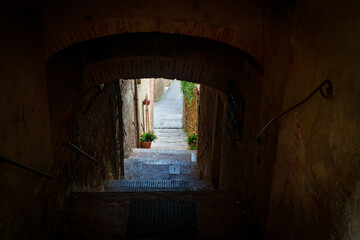 Dark vaulted passage with steps leading to sunlit alley, Tuscany