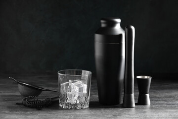 Different bartender utensils and glass with ice cubes on grey table against green grunge wall